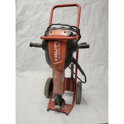 Red Hilti TE 3000-AVR jackhammer on wheels, positioned on a wrinkled white surface. It shows signs of wear, indicating frequent use.